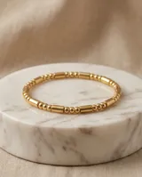 Pulsera esclava de acero con baño de oro, compuesta por una secuencia de cuentas esféricas y cilíndricas pequeñas.