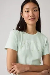 Remera de algodón color verde menta, con cuello redondo y mangas cortas. Presenta el logo de la marca estampado en el frente con detalles de pequeñas flores bordadas.