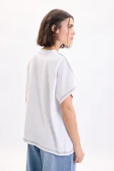 Camiseta blanca de manga corta con corte holgado y costuras decorativas con pespuntes en color negro.