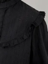 Blusa color mostaza con textura de pequeños puntos y detalles calados verticales. Presenta cuello alto con volados, volados decorativos en los hombros y mangas largas con puños elastizados.