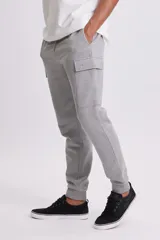 Pantalón deportivo tipo jogger en color gris claro, con diseño cargo que incluye bolsillos laterales. Presenta cintura elástica con cordón ajustable y puños elásticos en los tobillos.