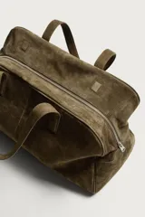 Bolso de viaje de diseño minimalista confeccionado en piel con acabado serraje. Cuenta con compartimento principal con cierre de cremallera e imanes, interior con bolsillos organizadores y doble asa de mano en piel.