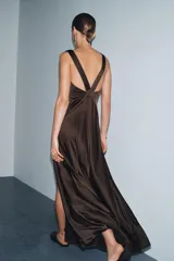 Vestido largo de satén color marrón oscuro, con escote en pico pronunciado, tirantes anchos y bajo en línea evasé con abertura lateral.