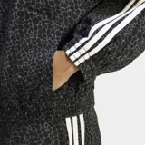 Campera Adidas Firebird AOP extragrande, de tejido denim con estampado animal print en tonos grises y negros. Presenta cuello alto, cierre frontal completo, bolsillos laterales y las clásicas tres tiras blancas de la marca en las mangas.
