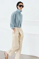 Pantalón de tiro medio confeccionado en algodón, con diseño cruzado en la cintura y cierre frontal con botones. Presenta trabillas para cinturón, bolsillos laterales ocultos y un bolsillo frontal con solapa y botón.