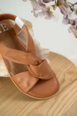 Sandalias chatitas de cuero en tono nude, con diseño de tiras cruzadas en el empeine y elástico en el talón para mayor ajuste. Presentan una plantilla acolchada y detalles en cuero charolado en la parte posterior.