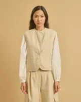 Chaleco corto color beige, con cuello redondo, cierre frontal con un botón y dos bolsillos delanteros.