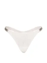Tanga de encaje color blanco con tiras brillantes decoradas con pedrería y el logo de Victoria's Secret.