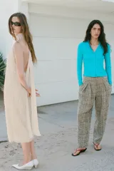 Vestido largo color crudo de cuello halter, sin mangas y con textura de flecos en toda la prenda. Cuenta con espalda descubierta, cierre de botones y lazada a contraste.