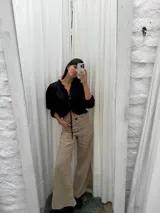 Blusa negra de lino con acabado brillante, de manga larga abullonada, escote con volados y cierre frontal con tiras para anudar.
