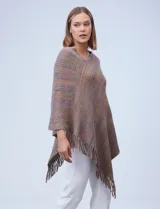 Poncho tejido en hilo soft, con efecto jaspeado multicolor (predominantemente tonos oscuros como azul marino, negro, y toques de violeta y dorado/lurex). Presenta un diseño asimétrico y flecos largos en los bordes.