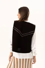 Chaleco oversize confeccionado en cuero descarne, con diseño de terminación en picos. Presenta lazos frontales con ojalillos metálicos y detalle de tachas metálicas en hombros y espalda.