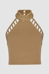 Top cropped color beige confeccionado en punto crepé, con cuello halter adornado con apliques dorados y aberturas caladas en los hombros.