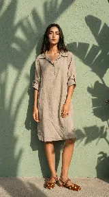 Vestido camisero midi de lino color beige, de calce relajado, con cuello clásico, cierre frontal parcial con botones, mangas 3/4 regulables y bolsillos delanteros.