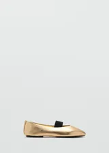 Zapato plano tipo bailarina en color dorado, con punta redonda y tira elástica en color negro sobre el empeine.