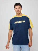 Remera de algodón con corte raglán, cuerpo azul marino y mangas cortas amarillas. Presenta un estampado frontal con el logo de la marca Rusty en tipografía estilizada en blanco con borde amarillo.