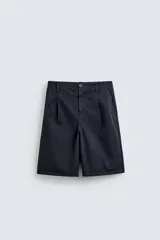 Bermuda de corte relajado confeccionada en denim de algodón rígido, con pliegues frontales, bolsillos laterales y bolsillos traseros de vivo. Cuenta con cierre frontal de cremallera y botón.