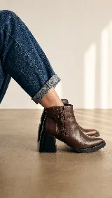 Bota corta de cuero marrón con diseño de paneles laterales texturizados. Presenta un taco ancho cuadrado en color negro y suela de plataforma baja, ofreciendo un estilo moderno y estable.