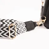 Bandolera negra de cuero sintético con correa ancha de tela estampada en blanco y negro.
