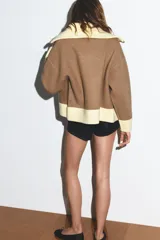 Chaqueta de punto con cierre frontal de cremallera, cuello alto, manga larga y bolsillos delanteros de plastrón. Presenta un diseño bicolor en tonos marrón y amarillo claro en cuello, puños y ruedo.