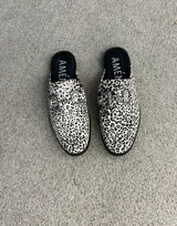 Suecos tipo mocasín de cuero metalizado plateado, con detalle de estribo metálico en el empeine y suela plana negra.