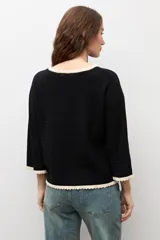 Sweater de punto negro con escote bote, mangas largas y detalles de terminación en ondas de color blanco en el cuello, los puños y el ruedo.