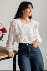 Camisa blanca de manga larga con detalles de volados en los hombros y bordado geométrico en el pecho. Presenta un diseño holgado con puños elásticos.