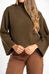 Polera de lana oversize color beige melange, con cuello alto, mangas largas acampanadas y diseño de tejido acanalado con tramas direccionales.