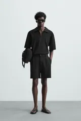 Bermuda de hombre color verde claro, de corte regular y tiro medio, con pinzas frontales, bolsillos laterales y bolsillos traseros de vivo. Cierre frontal con botón y cremallera.