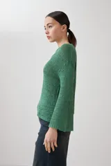 Sweater de punto fino en color verde, con cuello redondo y mangas largas. Presenta un detalle integrado de pañuelo estampado con motivos florales en la parte inferior, que se cruza sobre la cintura.