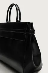 Bolso de mano extragrande negro de cuero sintético, con compartimento principal con cierre de imán, bolsillo interior con cierre y bolsillo secundario con solapa y detalle de cinta. Cuenta con dos asas de mano.