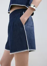 Short de denim azul oscuro de tiro alto, con bolsillos y detalle de bordado blanco en el borde inferior.