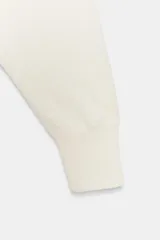 Jersey de punto color blanco crema, con escote en pico, manga larga y sisa ancha terminada en puño.