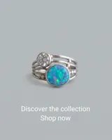 Anillo de plata 925 con diseño multicapa, decorado con una piedra central de ópalo sintético en tonos azules y verdes, y una piedra redonda translúcida más pequeña en la parte superior.
