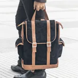 Mochila de cuero vacuno color negro con detalles en marrón. Tiene un bolsillo con broche a presión a cada costado y un bolsillo con cierre en la parte trasera. El interior está forrado en tela y tiene un bolsillo con cierre y otro pequeño para el celular.