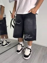 Bermuda baggy de denim color negro con efecto lavado, corte holgado y largo por debajo de la rodilla. Cuenta con bordados en hilo blanco con las frases "stay real" y "Built different" en las piernas.