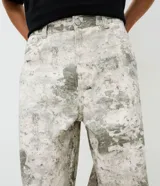 Pantalón de sarga de algodón con corte super baggy, tiro bajo y piernas ultra amplias. Presenta un estampado integral con efecto marmorizado o dirty, bolsillos utilitarios laterales, bolsillos frontales y traseros, cintura con pasantes y cierre frontal con botón y cremallera.