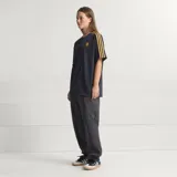Camiseta de fútbol Adidas del Manchester United, modelo Terrace Icons. Diseño negro con sutiles rayas verticales moradas, franjas amarillas en los hombros y detalles bordados en dorado, incluyendo el trébol de Adidas y el escudo clásico del club.