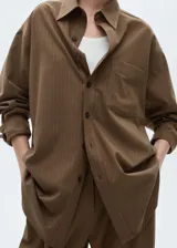 Camisa oversize de corte recto con diseño de raya diplomática, cuello camisero, cierre frontal de botones y bolsillo de parche en el pecho.