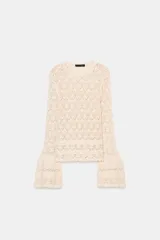 Jersey de punto color crema, con cuello redondo y manga larga acampanada. El tejido presenta un calado con patrón de rombos.