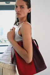 Bolso de hombro formato maxi de piel, en combinación de colores rojo y bordó. Cuenta con detalle de pespuntes, bolsillo interior con cremallera extraíble y cierre mediante fruncido con asas finas de hombro.