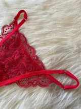 Conjunto de lencería compuesto por bralette de encaje con breteles regulables, tanga regulable y portaligas con volados en las caderas.