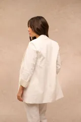 Blazer blanco de corte recto y largo medio, con solapas clásicas, bolsillos con solapa en el frente y mangas largas con vuelta estampada a rayas.