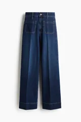 Jean de denim azul oscuro con tiro alto y corte wide leg de pierna ancha. Cuenta con bolsillos de parche delanteros y costuras pespunteadas a contratono.