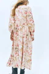 Vestido largo de mezcla de viscosa en color beige con estampado floreado. Presenta un escote en V pronunciado, botonadura frontal con botones forrados, y mangas largas abullonadas con puños ajustados. Cuenta con costuras fruncidas bajo el busto y en la cintura, dando paso a una falda de corte fluido y leve vuelo.