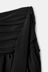 Falda pantalón de tiro medio color negro, con diseño de volantes y tejido asimétrico lateral que incluye un lazo colgante. Cuenta con cierre lateral de cremallera oculta.