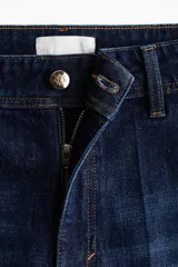 Jean ancho de tiro alto confeccionado en denim de algodón con ligero stretch, de color azul oscuro con efecto deslavado y pliegues frontales.