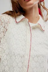 Camisa crop de encaje floral semitransparente, color blanco, con mangas cortas y ribetes en color contrastante.