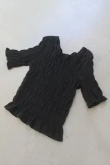 Remera negra de algodón con textura fruncida en todo el cuerpo y mangas cortas con terminación de volado.