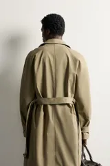 Trench regular fit de color beige, confeccionado en tejido técnico repelente al agua, con diseño de botonadura cruzada, cuello con solapas, mangas raglán con trabillas ajustables en los puños y cinturón del mismo tejido.